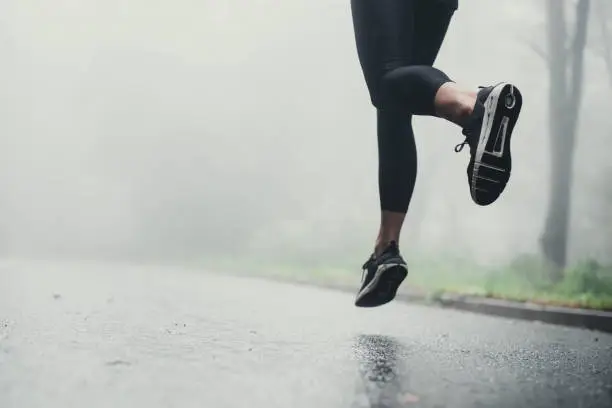 Photo of Unrecognizable athlete jogging on the road during rainy day.