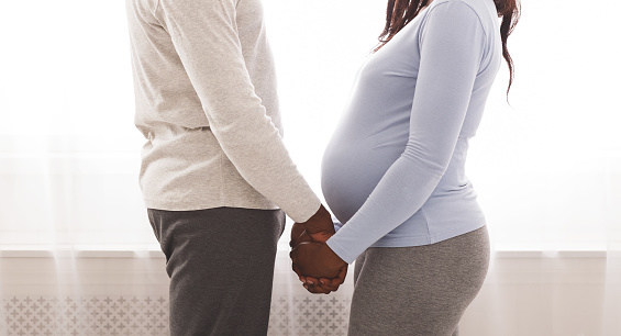 Cropped image of african pregnant couple holding each other hands next to window