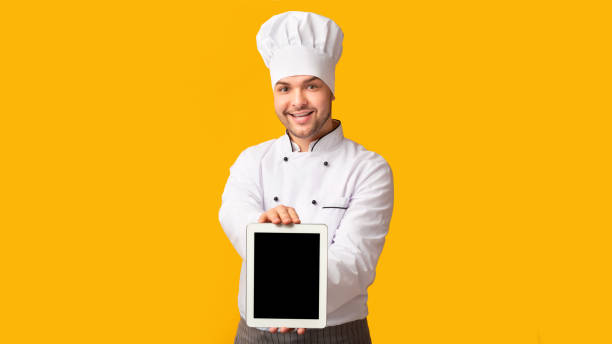 istock Chef Man Showing Tablet Empty Screen Standing, Yellow Background, Panorama 1199401562