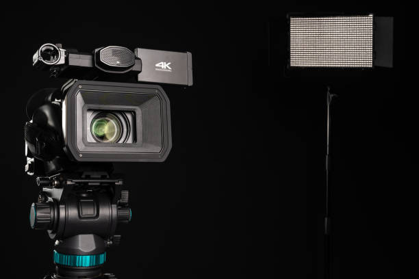 istock Professional 4K video camera on camera tripod and lighting LED panel on black background 1199401584