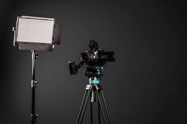 istock Professional cinema video camera on a camera tripod and one lighting LED panel on black studio background 1199402307