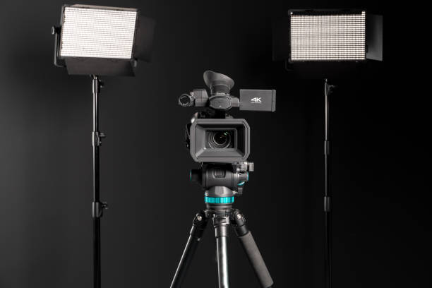 istock Professional  video camera on camera tripod and two lighting LED panel on black background 1199402411