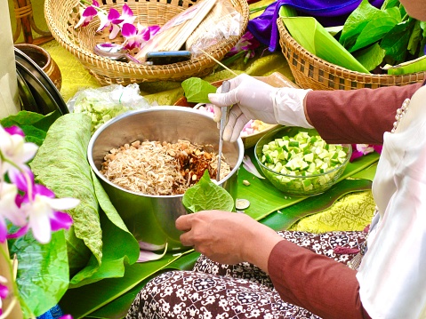 Thai Traditional Snack and Dessert, Woman Cooking Miang Kum or Sweet and Spicy Betel Leaf and Lotus Petal Wrap Filled with Coconut, Peanuts, Dried Shrimp, Chiles and Lime.