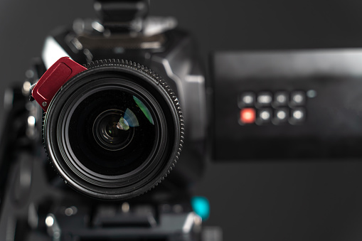 Professional video cinema camera on a camera tripod on black studio background copy space, lens close-up. The picture is taken with Sony A7III camera.