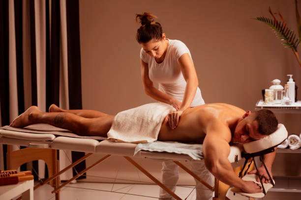 femme de thérapeute de massage faisant le massage curatif. homme appréciant dans le massage relaxant au traitement de spa de santé. - massage table photos et images de collection