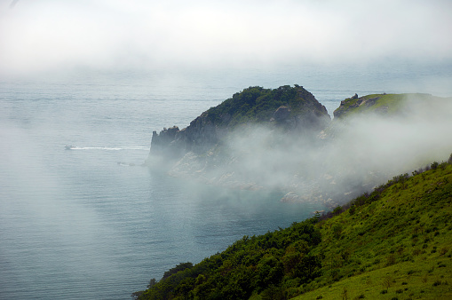 Steep cliff above the sea in the fog. The rocky shore of the sea.