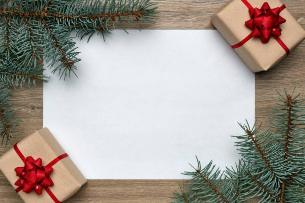 istock Christmas or New Year composition. White sheet of paper with copy space, gift boxes and Christmas tree branches on wooden background. Flat lay, top view, horizontal layout 1199408357