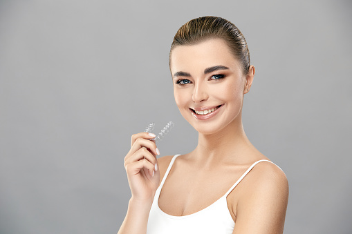 beautiful blond woman holding invisible braces in hand and smiling to the camera, stomatology concept, healthy and perfect smile