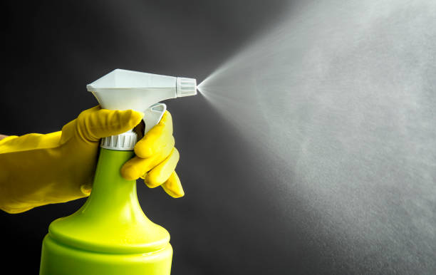 femme utilisant des gants en caoutchouc jaunes utilisant la bouteille verte de jet et pulvérisant la brume liquide dans l'air, effet d'éclairage frais. beaucoup d'espace de copie. - spary photos et images de collection