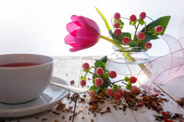 Cup of hot aromatic fruit tea in a floral decoration on white vintage wooden table. Close up.