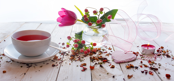 Cup of tea on mothers day with aromatic fruit tea. Floral decoration with pink heart on white vintage wooden table.