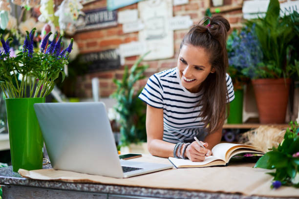 istock Joyful florist looking at laptop with client orders and writing them down in notebook 1199418913