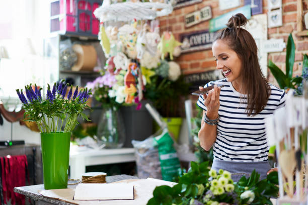 istock Young cheerful florist speaking on phone with client while standing at the counter 1199419135