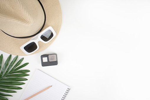 Flat lay travel accessories for young women with hats, glasses, and books on a white table and summer leaf. With copy space.