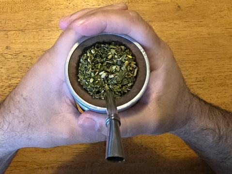 Closeup of the hands of a man holding a typical container for yerba mate consumption in South America.