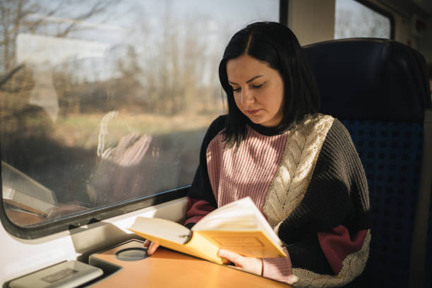 istock Young woman reading a book while traveling by train 1199424342