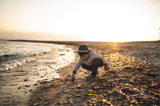 Little boy standing on beach and throwing stones into sea