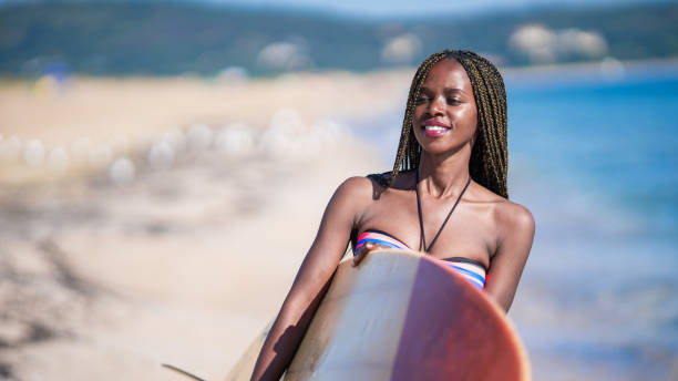 istock African woman holding surfboard and walking on beach 1199430653