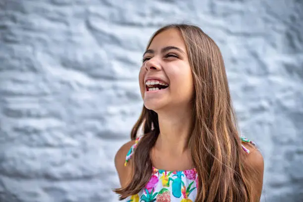 Photo of Portrait of a laughing cute girl in front of a white stone wall.