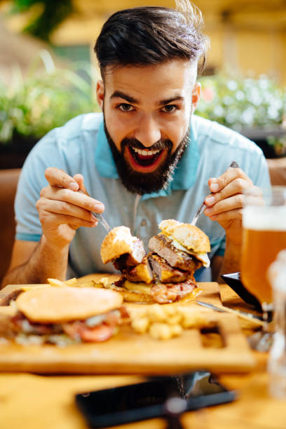 istock Young man eating oversized burger in a fast food restaurant 1199434214