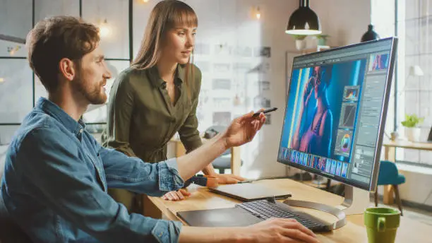 Female Art Director Consults Designer Colleague, They Work on a Portrait in Photo Editing Software. They Work in a Cool Office Loft. They Look Very Creative and Cool.