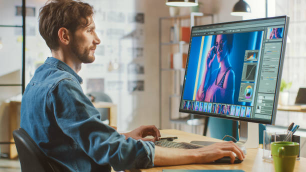 ひげとジーンズシャツを持つ美しい創造的な男性のビデオエディタは、ビッグディスプレイで彼のパーソナルコンピュータ上の映像で動作します。彼はクールな明るいオフィスロフトで働い� - digital photography ストックフォトと画像
