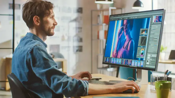 Beautiful Creative Male Video Editor with Beard and Jeans Shirt Works with Footage on His Personal Computer with Big Display. He Works in a Cool Bright Office Loft.