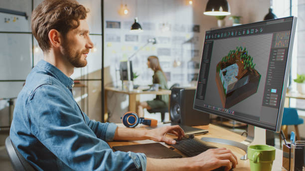 istock Beautiful Male Working in an Urbanistic Programm Creating 3 visualisation on His PC with Big Display. He Works in a Cool Office Loft. Other Female Creative Colleague Works in the Background. 1199435190