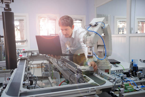 Engineer holding product to teach robot arm position of program and checking on laptop for smart factory automation stock photo