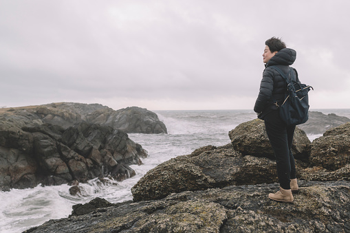 an asian chinese female traveler standing on the rock at seaside with strong wind and waves in iceland