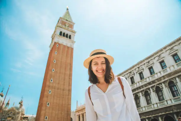 smiling pretty caucasian woman rise up hands at venice city square bell tower campanile di san marco on background