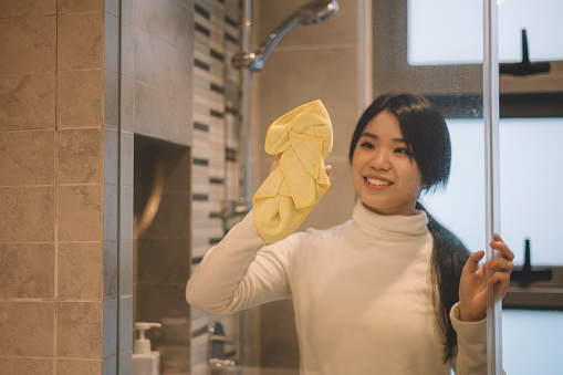 an asian chinese teenage girl cleaning up her bathroom wiping it with a yellow clothe