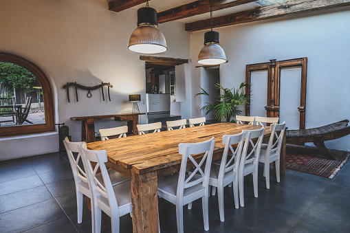 Wide angle view of dining area with large wooden table and chairs in traditional Spanish farmhouse featuring arched window, beamed ceiling, and slate flooring.
