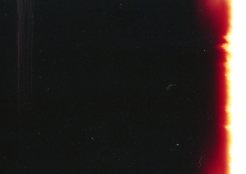A close-up scan of an old scratched 35mm color film with a beautiful red light leak strip grunge texture background.