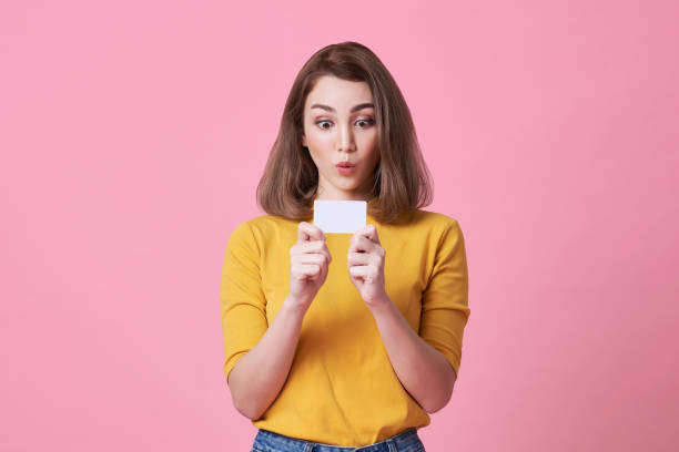 excited young woman in yellow shirt showing credit card isolated over pink background. stock photo
