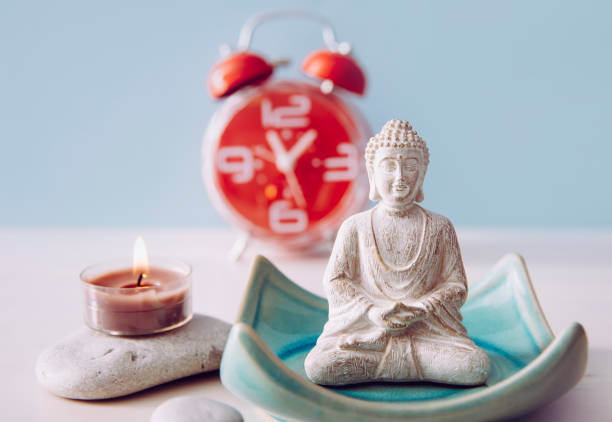 istock Finding time for self care and balance between body soul and mind. Balance between work and home concept. Lotus pose white color sitting meditation Buddha figurine, red alarm clock on background. 1199442993