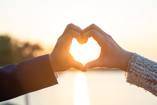 Women and men hands In the form of hearts against the sky through the sun's rays Hands in the form of love hearts