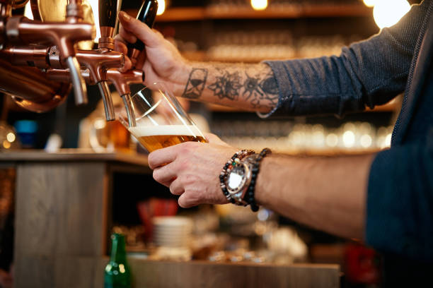 istock Tattooed caucasian barman pouring beer while standing in pub. Selective focus on hand. 1199444620