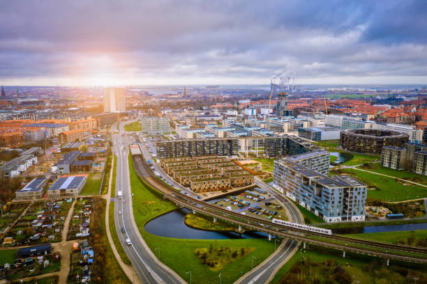 Copenhagen cityscape: Modern architecture at the sea HDR image of Copenhagen cityscape with contemporary office buildings and residental flats at Islands Brygge, Amager, shot with drone. Central in the image is the popular electricity driven subway that serves as public transportation for commuters. Here the metro train is captured above ground just before the tracks go underground. Dramatic cloudscape and lens flare in background. danish culture stock pictures, royalty-free photos & images