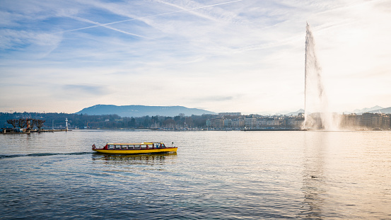 Lake Geneva panorama with the famous Jet d'Eau or water jet and small yellow shuttle boat in Geneva Switzerland