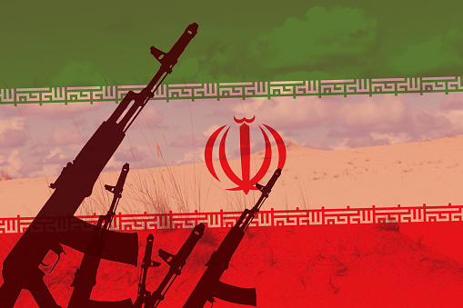 Toned background of the flag of Iran with a silhouette of a Kalashnikov AK-74 assault rifle against a sandy desert with sky, illustration