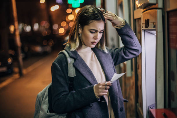 Young woman is upset in front ATM machine Worried woman with the hand on her forehead had problems with ATM machine exchange teller stock pictures, royalty-free photos & images
