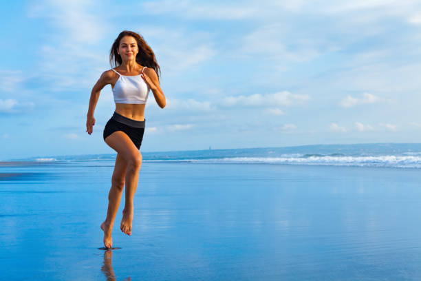 fille sportive fonctionnant par la plage le long du surf de mer - jumping women running vitality photos et images de collection