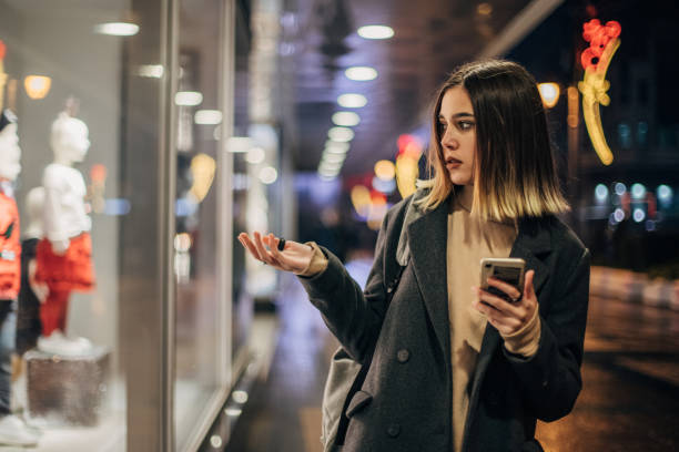 istock Women with mobile phone looking to store window 1199450761