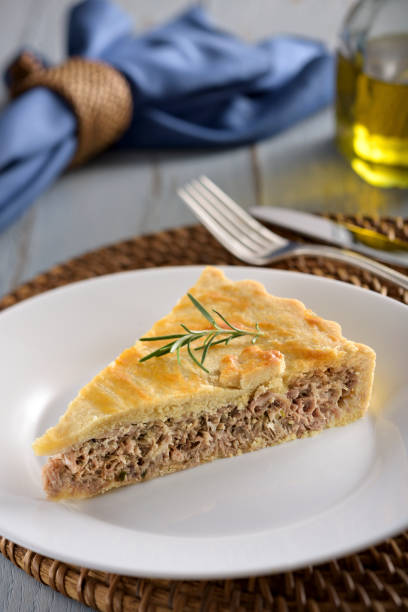 A slice of tuna fish pie A slice of tuna fish pie with a crispy golden-brown crust, on a white plate with fork and knife on the background. fish pie stock pictures, royalty-free photos & images
