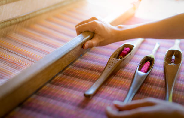 femme travaillant sur la machine de tissage pour tisser le tissu fait à la main. tissage textile. tissage à l'aide du métier à tisser traditionnel de tissage à la main sur des brins de coton. production de textileous ou de tissus en thaïlande. cultur - weaving machine photos et images de collection