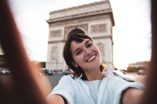 Young caucasian women walking in Paris in the city center talking and texting on the phone and commuting, exploring city landmarks, Tour Eiffel and Arc de Triomphe.