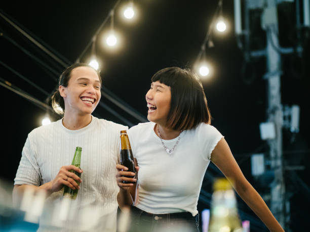 Young asian couple toasting with beer at rooftop party Young asian women toasting drinks with her boyfriend at a rooftop party. Young asian couple hanging out with drinks. woman drinking beer stock pictures, royalty-free photos & images