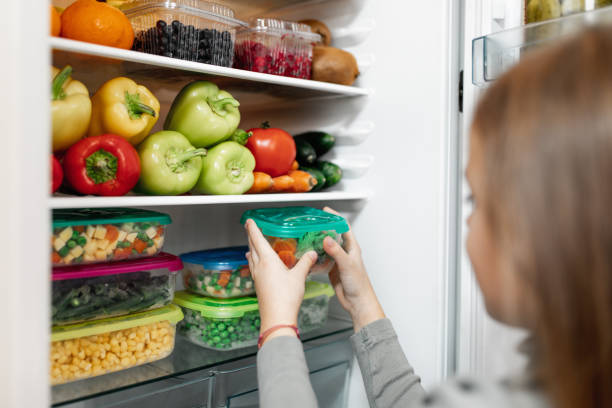 Girl taking raw food from refrigerator Adorable little girl taking containers with frozen mixed vegetables from refrigerator. happy green peas stock pictures, royalty-free photos & images