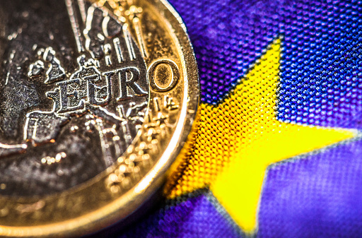 A close-up of a Euro coin, showing the word Euro over a map of Europe, next to a star from a flag of the European Union.